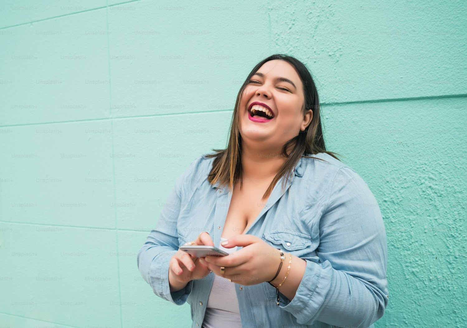 Woman laughing against a mint-green wall